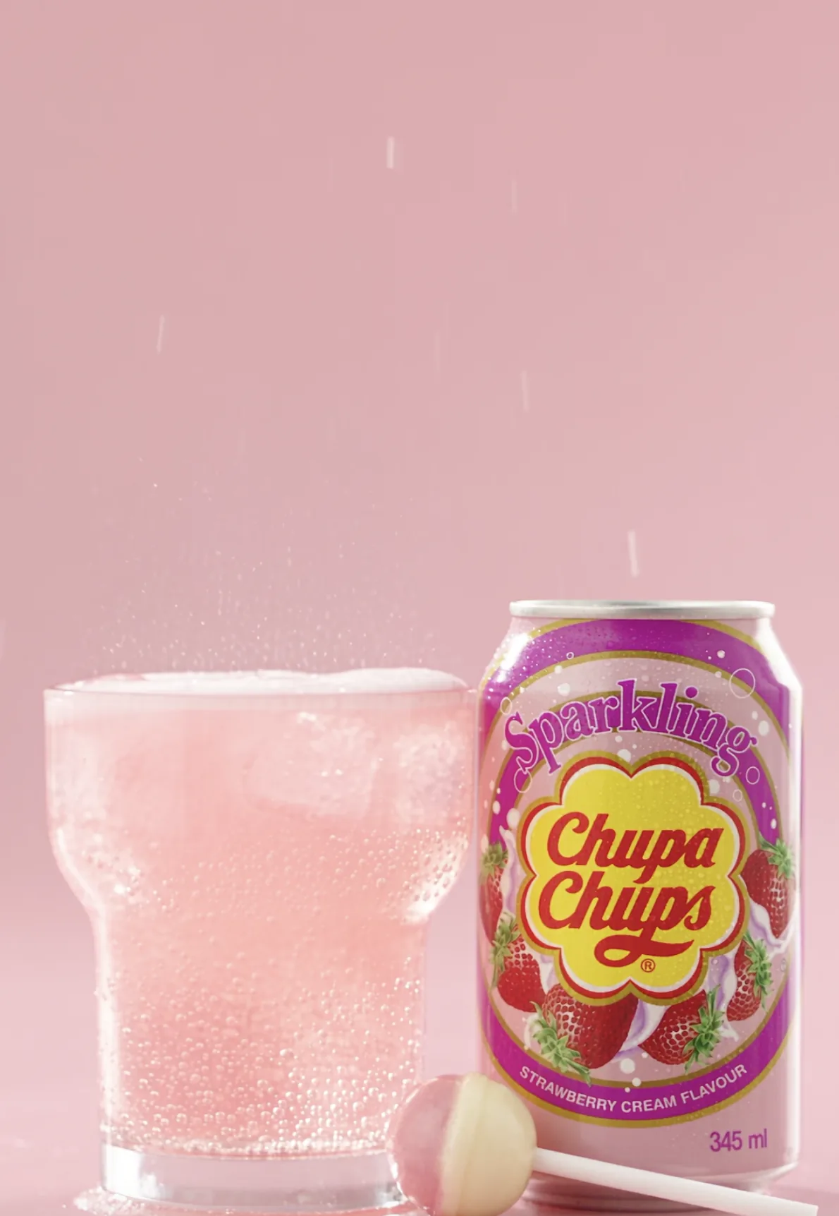 Pink sparkling drink next to a lollipop and soda can