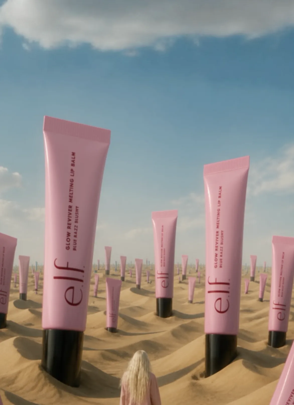 Giant pink lip balm tubes rising from desert dunes