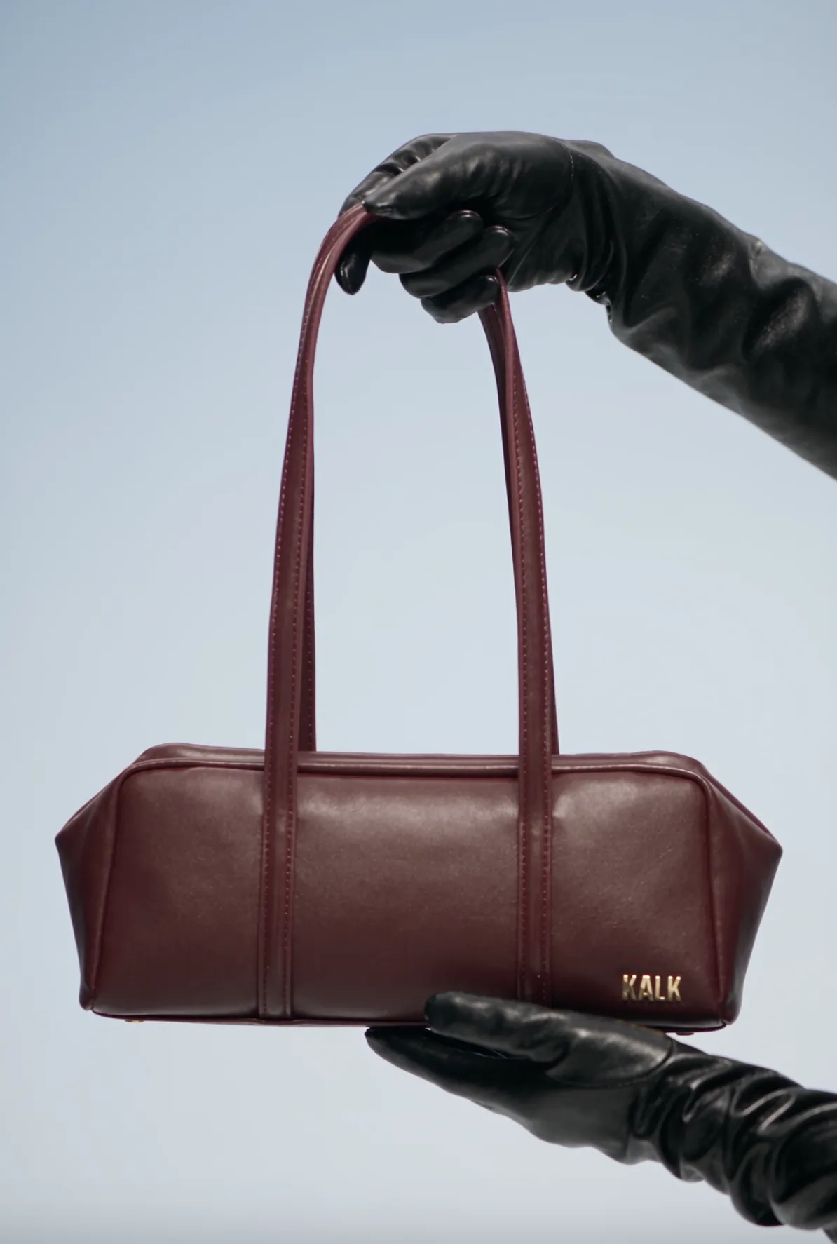 Burgundy leather handbag held by black-gloved hands