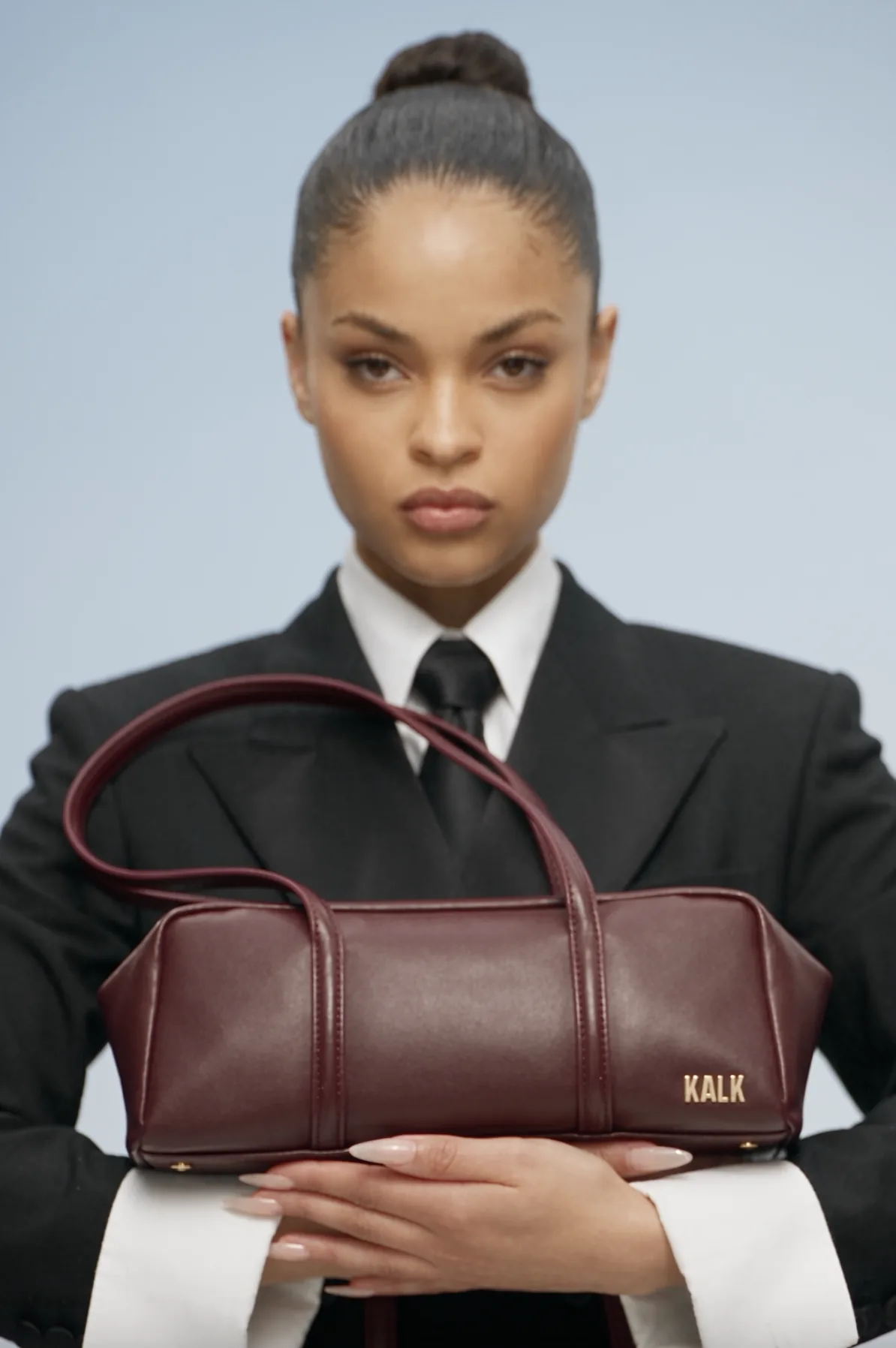 Model in a black suit holding a burgundy handbag