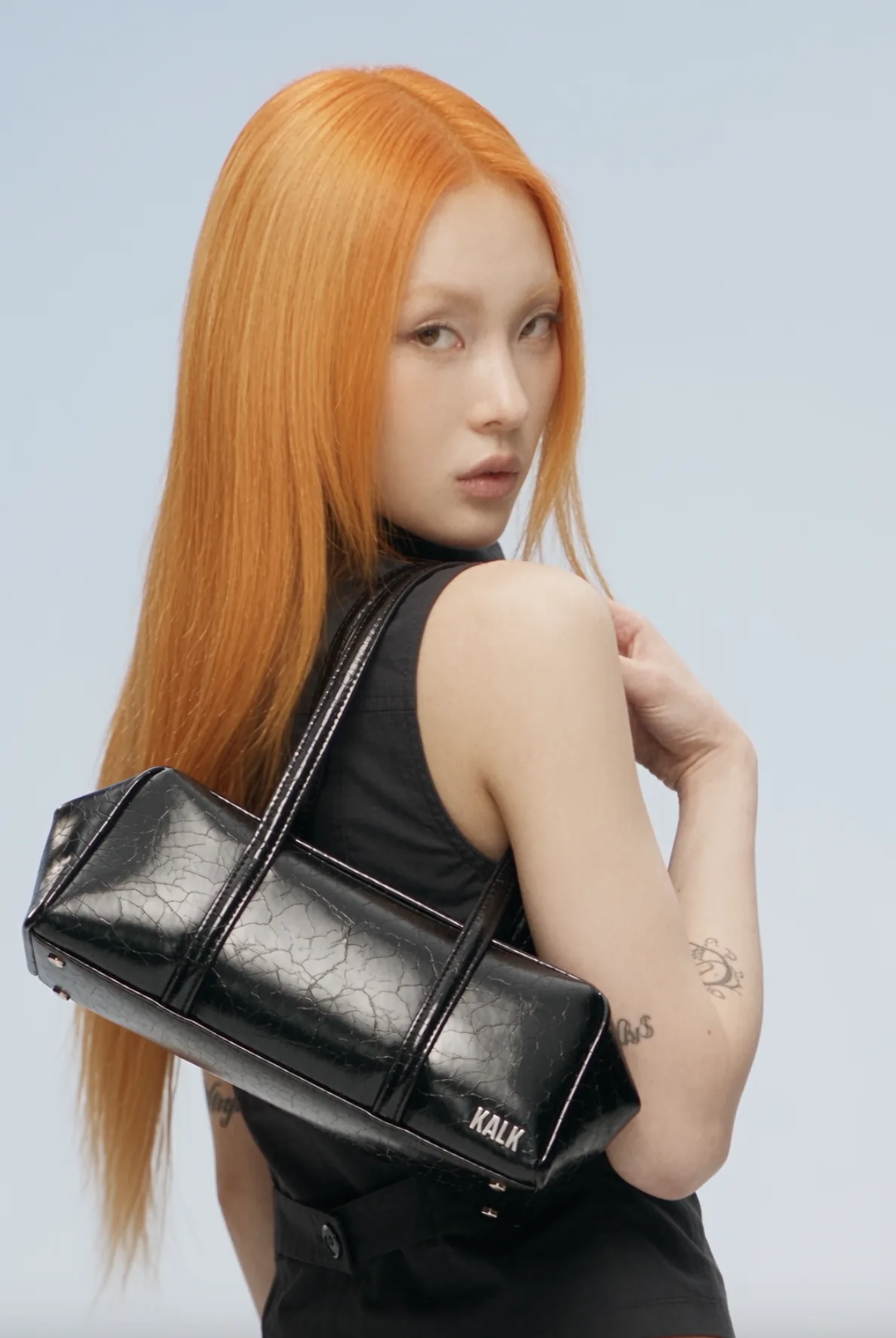 Model with orange hair carrying a black leather bag