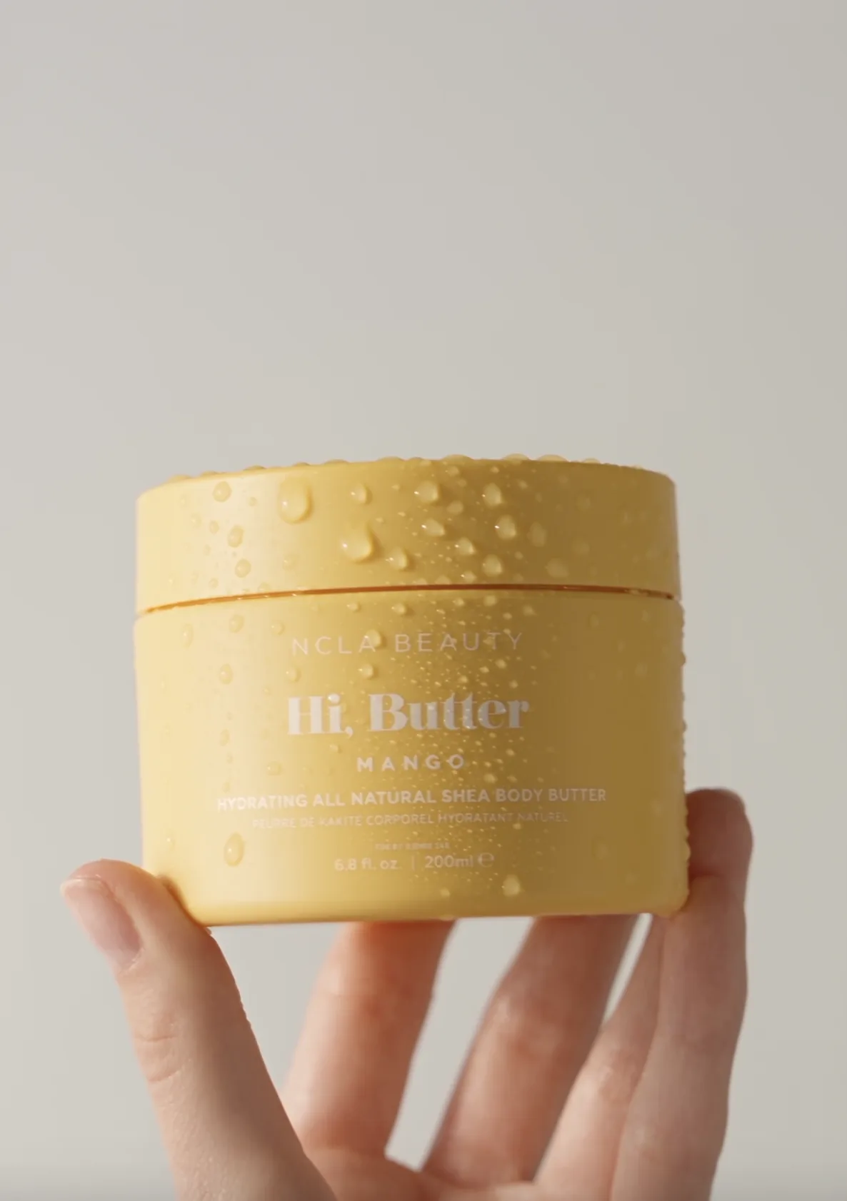 Hand holding a yellow jar of mango body butter